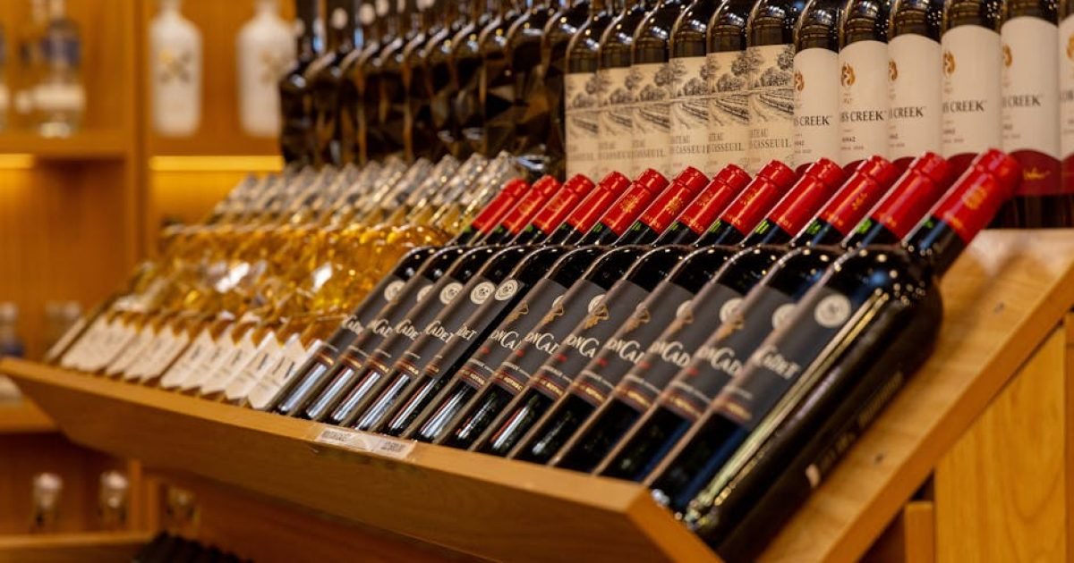Close de diversas garrafas de vinho dispostas em uma prateleira de madeira.