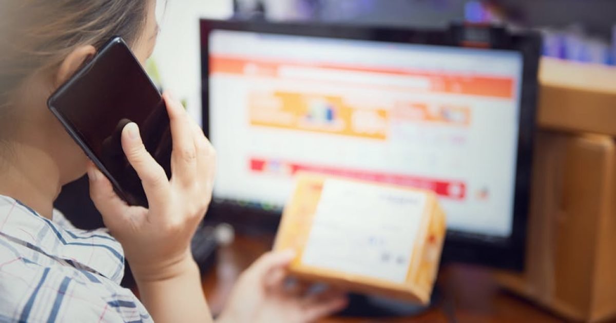 Mulher realizando várias tarefas ao mesmo tempo, usando um telefone e verificando um pacote de compra on-line em casa.