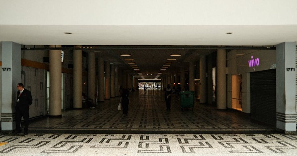 Corredor espaçoso em um shopping moderno com iluminação mínima e pessoas caminhando.
